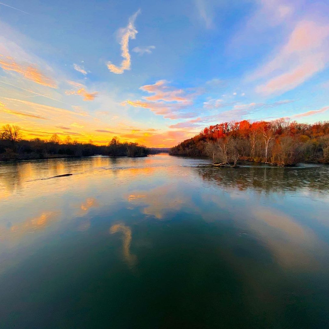 River reflecting colorful sunset, bordered by trees.