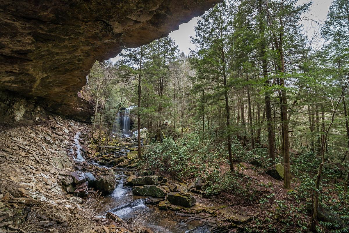 View from under a rock ledge showing a waterfall and forest.
