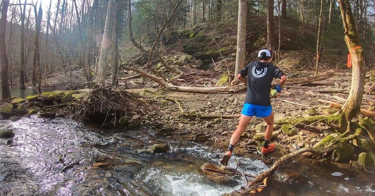 Trail runner crossing a forest stream.