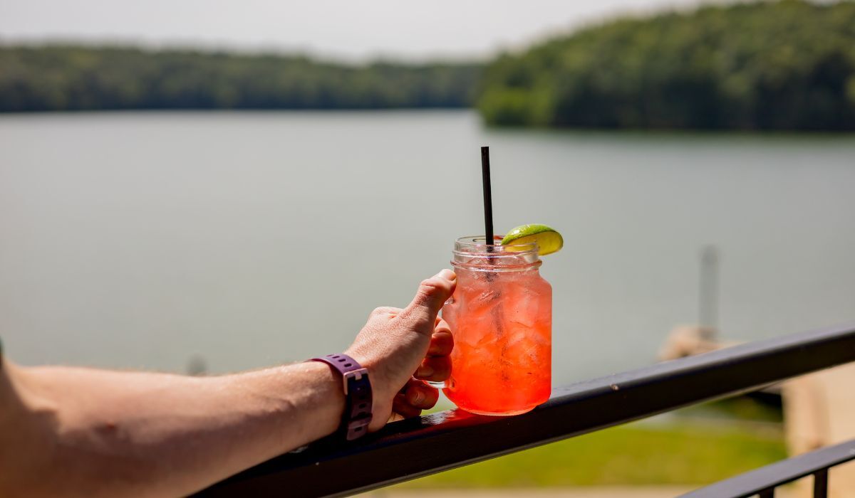 Hand holding a cocktail with a lake view in the background.