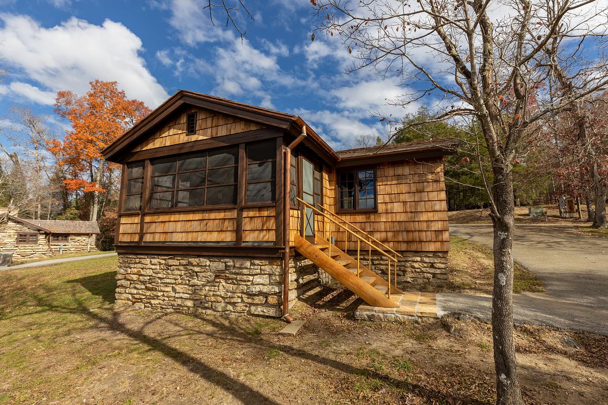 Rustic log cabin with stone foundation surrounded by bare trees.