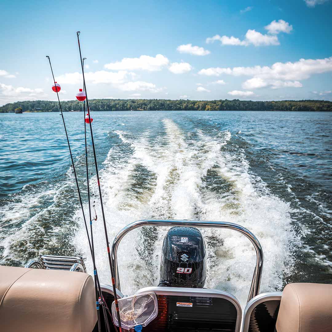 View from a boat's stern with fishing rods, speeding on a lake.