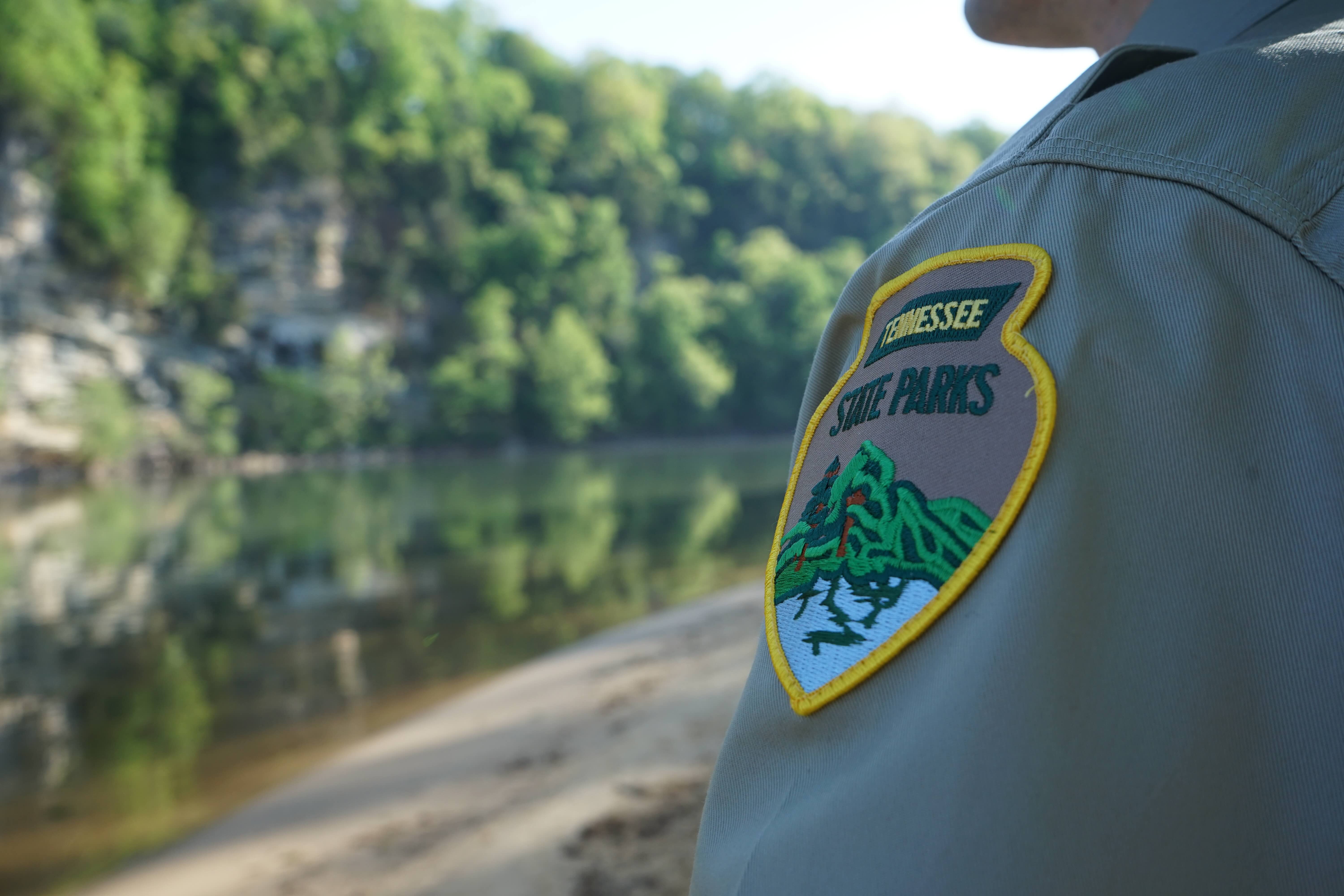 Park ranger's shoulder patch with a tranquil river landscape in the background.