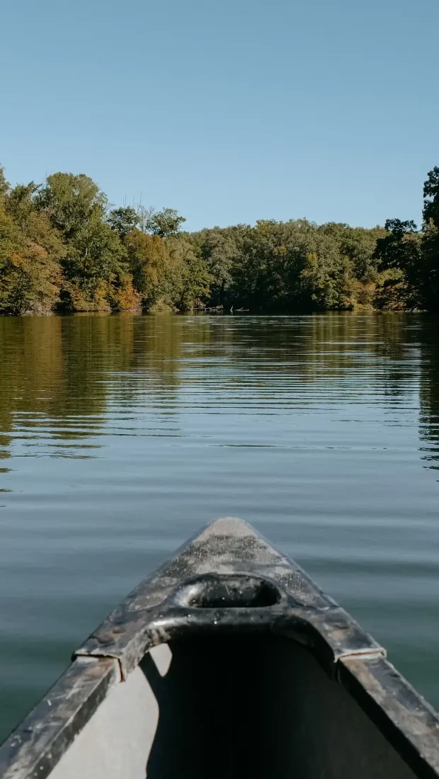 Canoe on calm lake surrounded by autumn trees under clear sky.