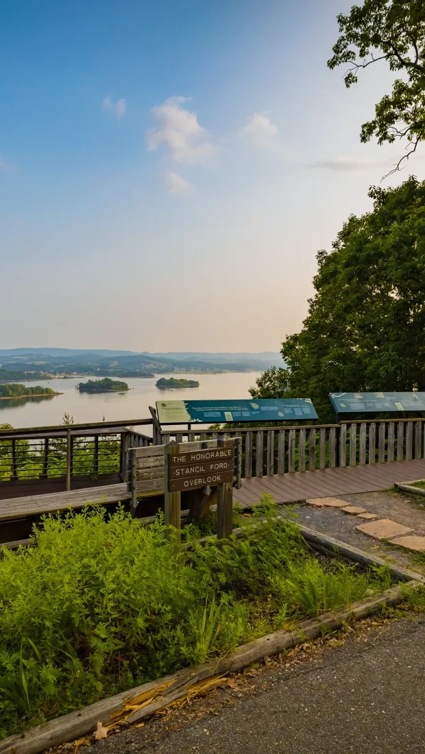 Scenic lake view from overlook deck with trees and informational signs.