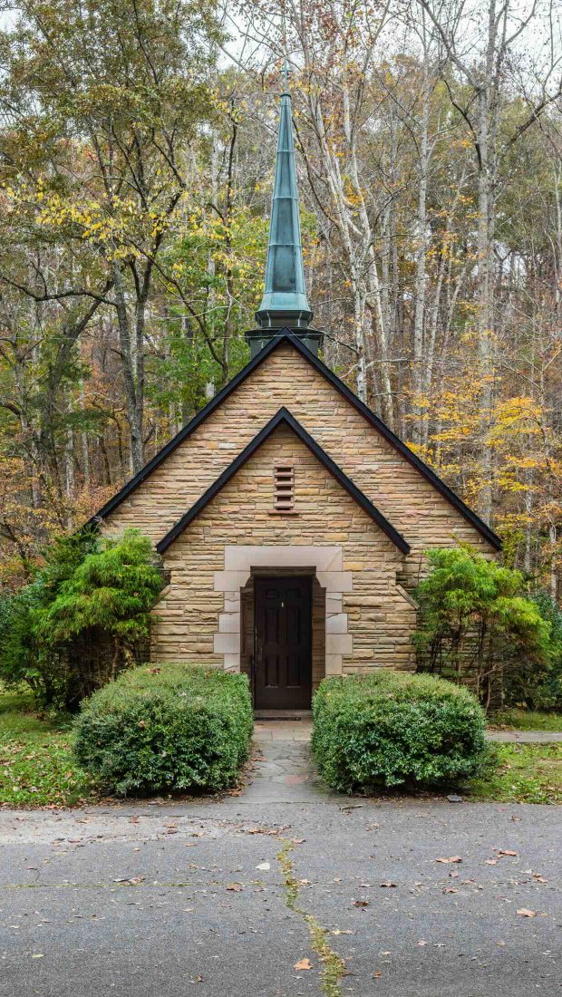 small church with bushes on the side and trees behind it