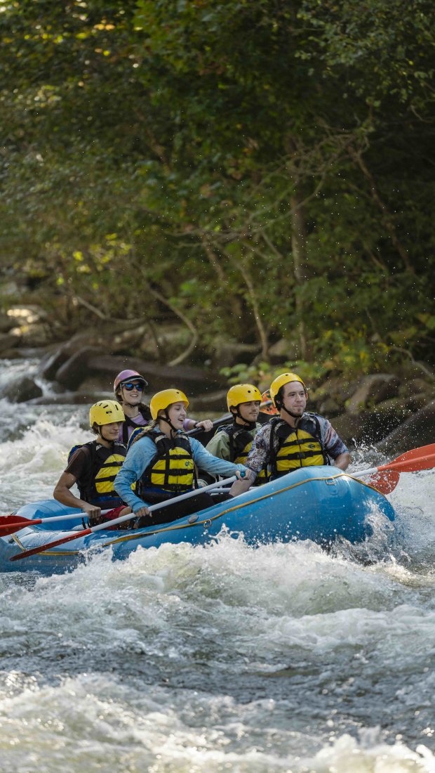 group of people wearing vests and helmets in a raft going down a river