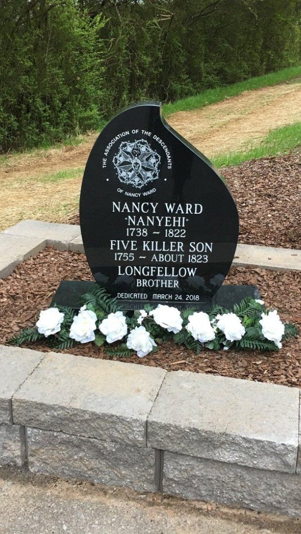 Black memorial plaque with white roses near a path.
