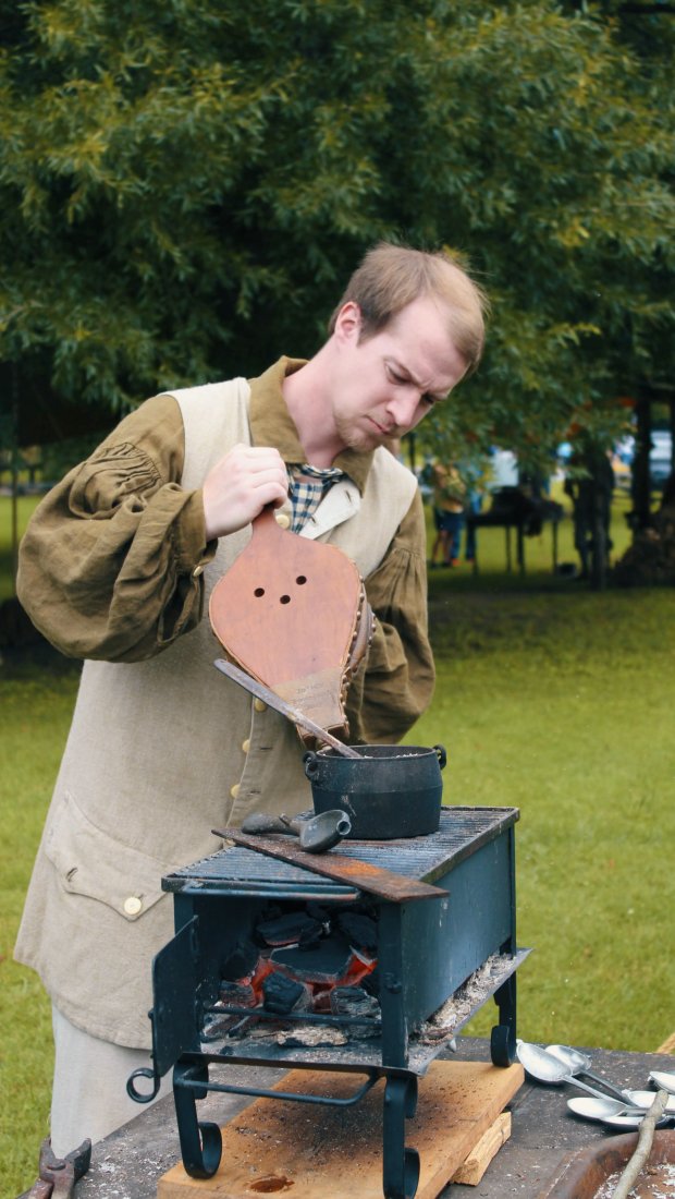 Man in medieval attire operating a small forge outdoors.