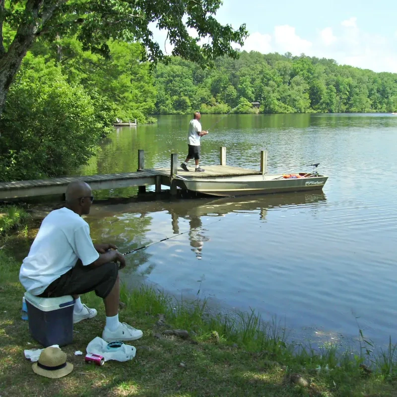 Two people fishing by a lake, one sitting and one standing on a dock.