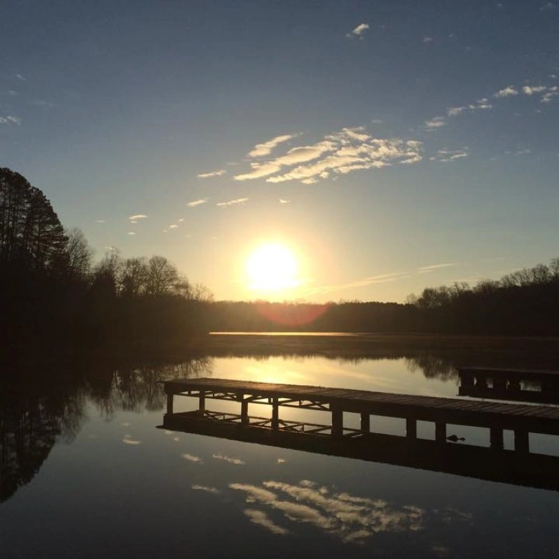 Sunset over a calm lake with a wooden dock and trees silhouetted.