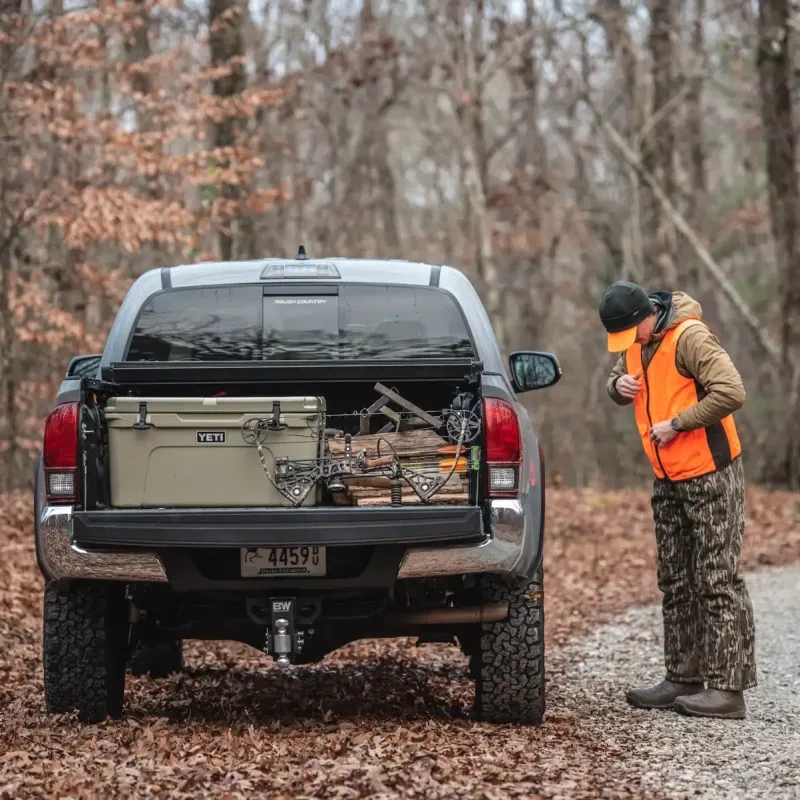 Truck in forest with gear, person in orange vest beside it.