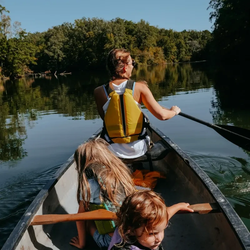 Three people canoeing on a calm river surrounded by trees.