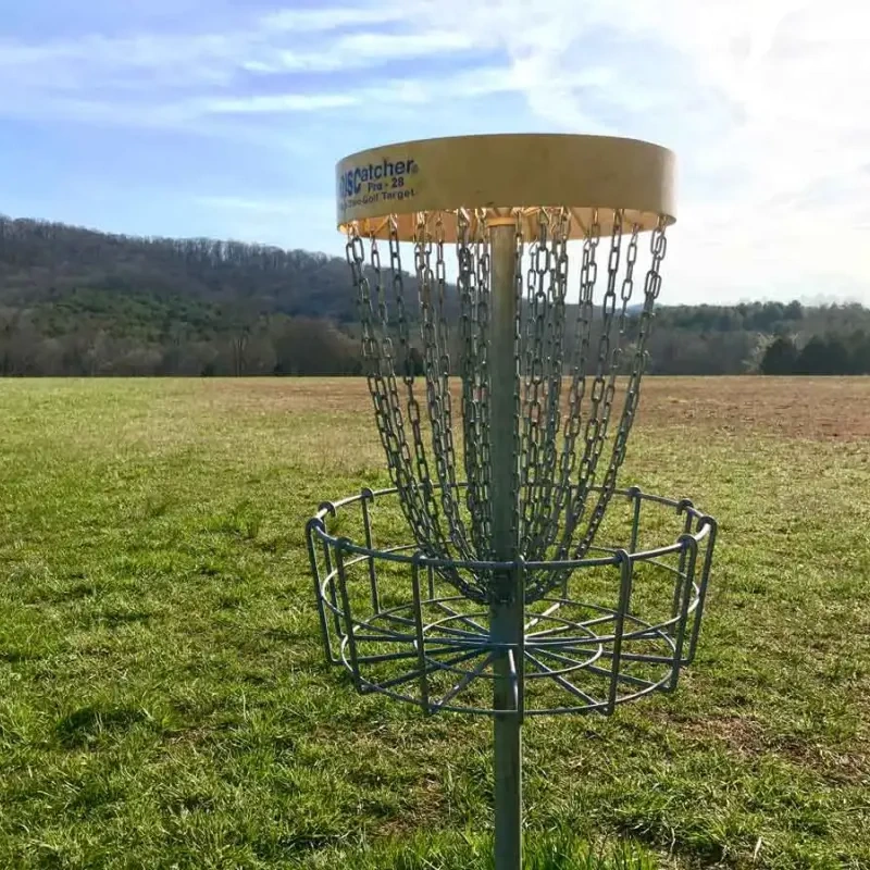 Disc golf basket on a grassy field with hills in the background.