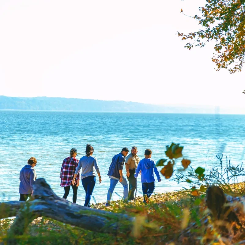 People walking along a lakeside path under a bright sky.