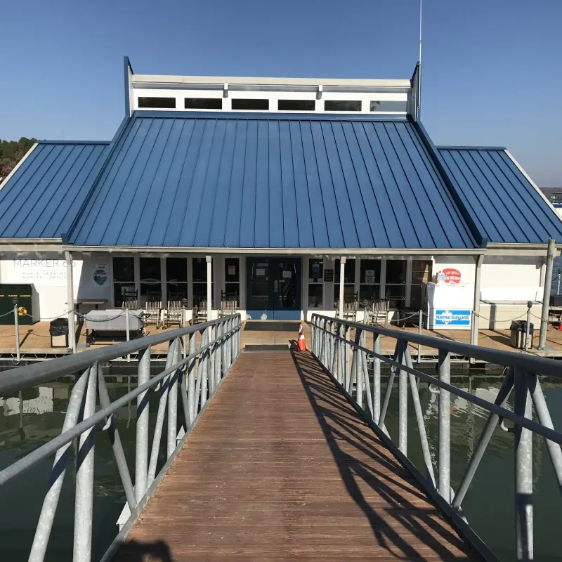 Wooden dock leading to a building with a blue roof on the water.