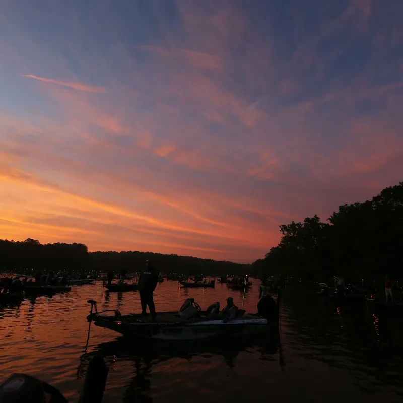 Sunset over a lake with boats silhouetted against vibrant orange and purple sky.