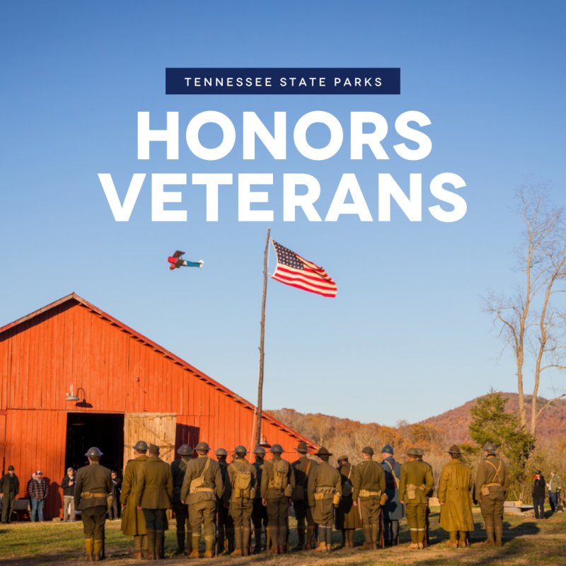 A group of uniformed individuals stands facing an American flag in front of a red barn. A biplane flies overhead. The text reads "Tennessee State Parks Honors Veterans."