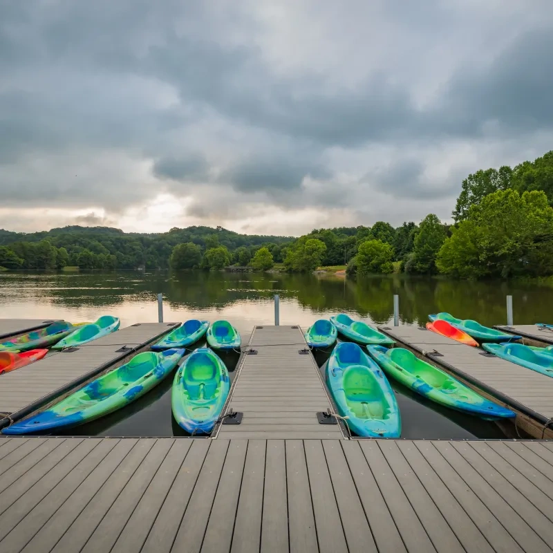 Colorful kayaks on a wooden dock, with a lake and cloudy sky in the background.
