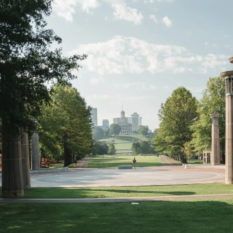 Stone pillars line a pathway with a city skyline and trees in the background.