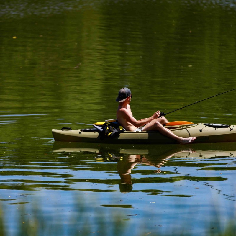 man shirtless with a hat fishing in small paddle boat
