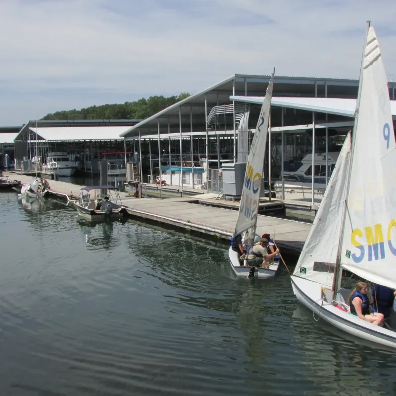 Sailboats docked at a marina with people boarding.