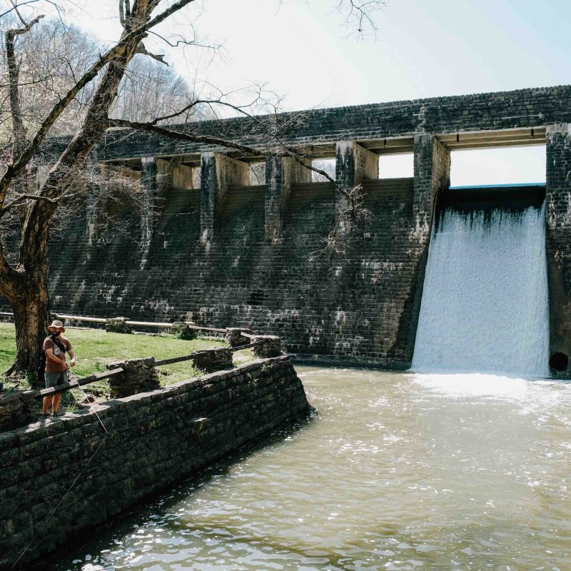two men fishing by a dam while standing on grass
