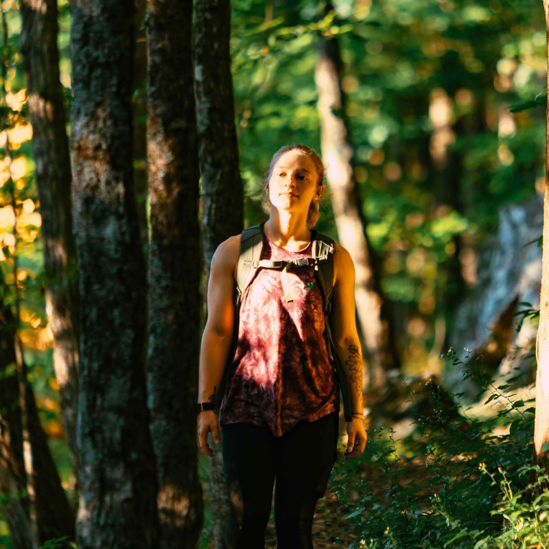 girl hiking in forest wearing a backpack and sun shining on her