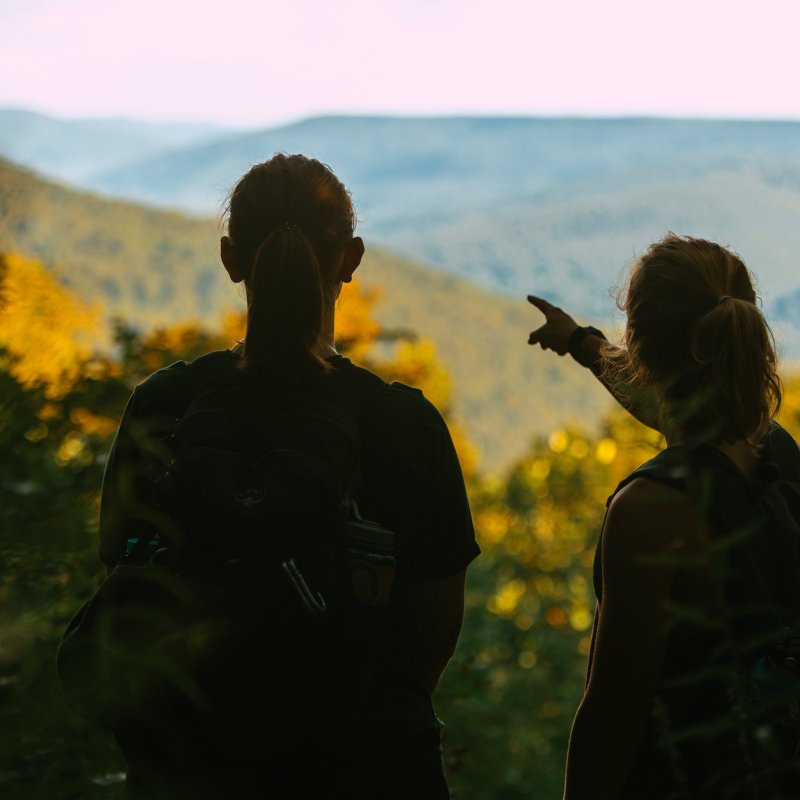view behind two girls looking at landscape on top of a cliff with one of them pointing