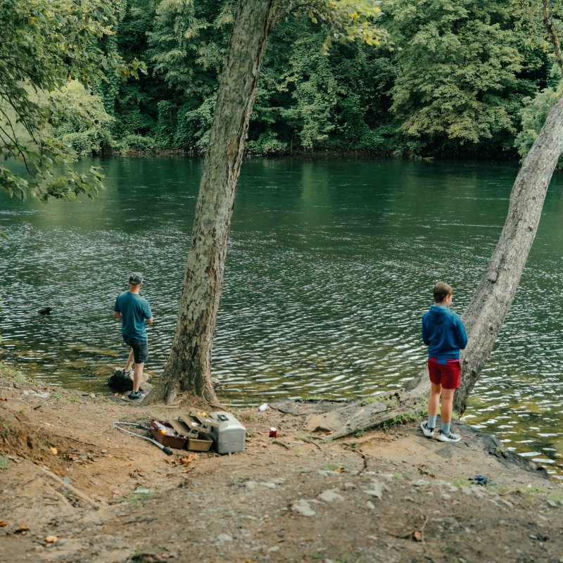 two people fishing in a river next to a swinging rope and a fishing kit near them