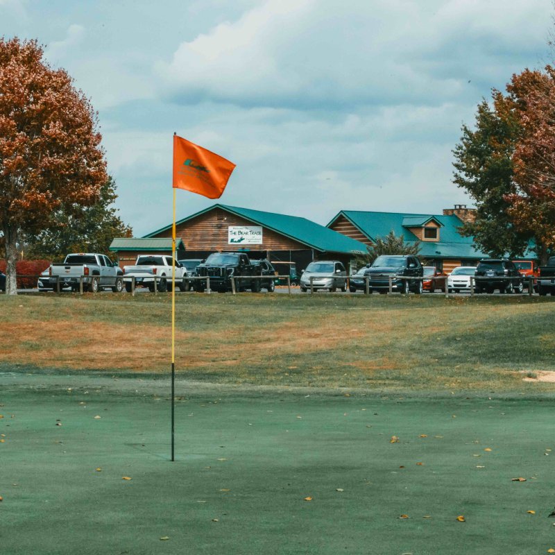Golf green with an orange flag and clubhouse in the background in autumn.