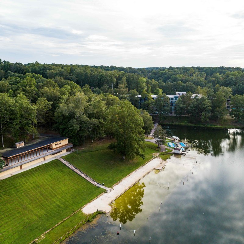 Aerial view of a lakeside park with trees, a beach, and small boats.