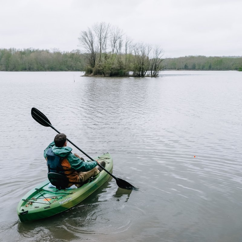 Person kayaking on a calm lake with overcast skies.