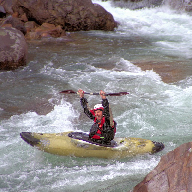 Kayaker navigating rough river waters between rocks.