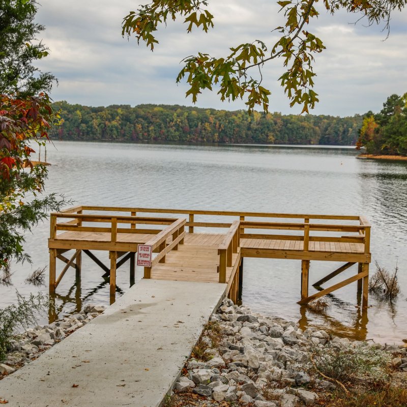 Wooden pier overlooking a tranquil lake surrounded by autumn trees.
