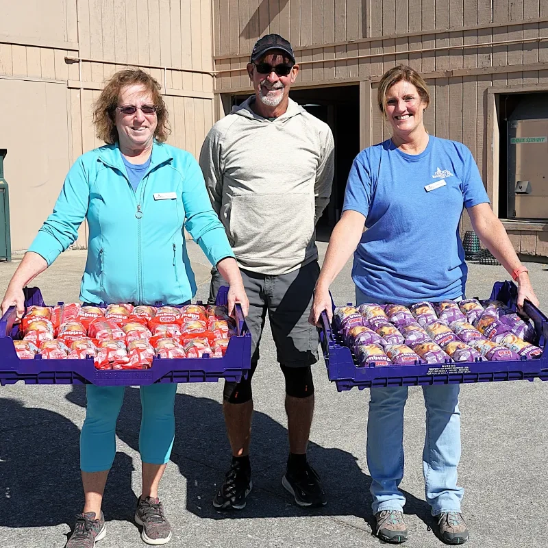 Three people standing outside a building. Two are holding trays of sandwiches.
