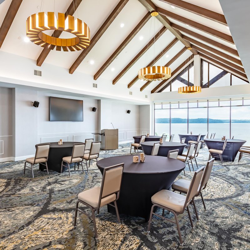 Modern conference room with ocean view, tables, chairs, and stylish lighting.
