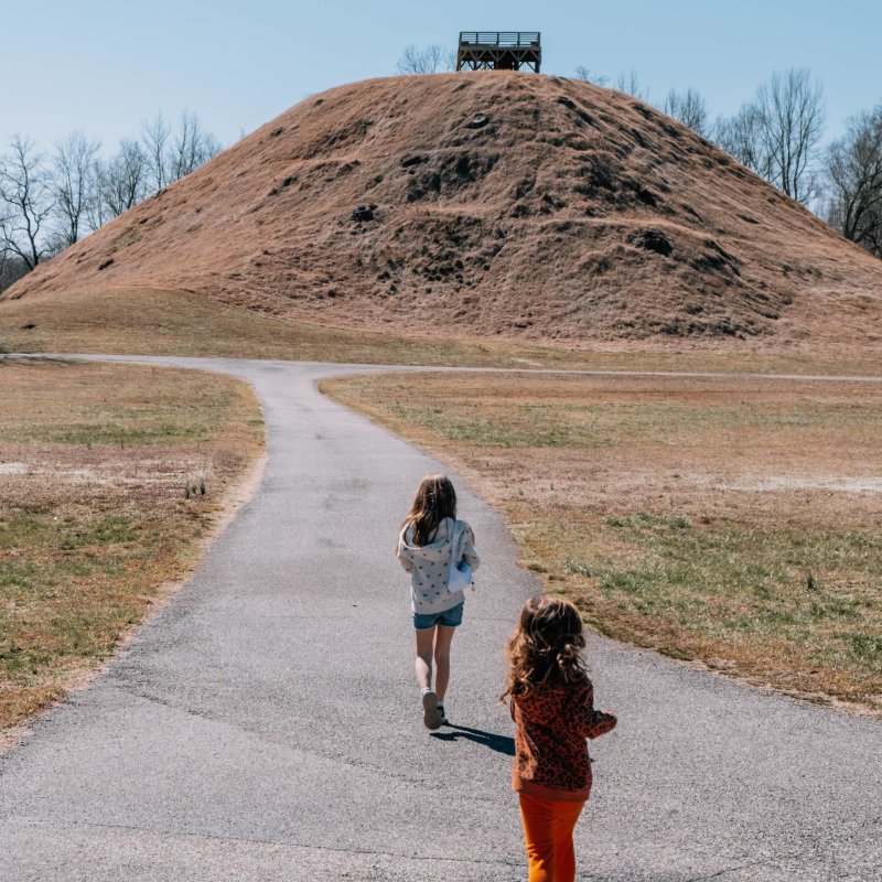 Two children walking towards a large mound on a sunny day.