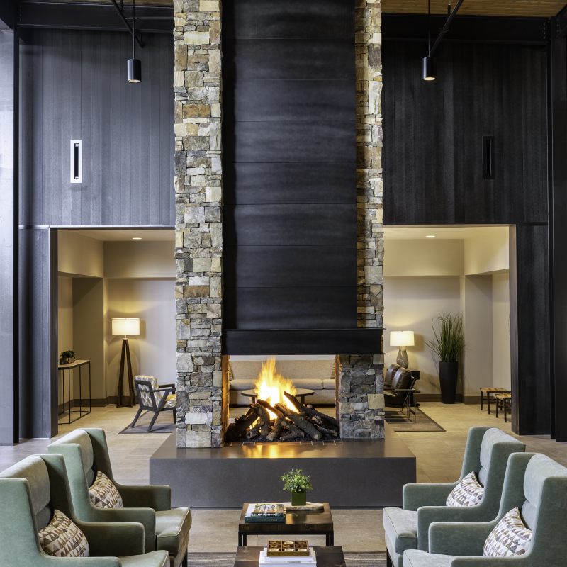A cozy lodge lobby with four chairs around a coffee table with an indoor stone fireplace.