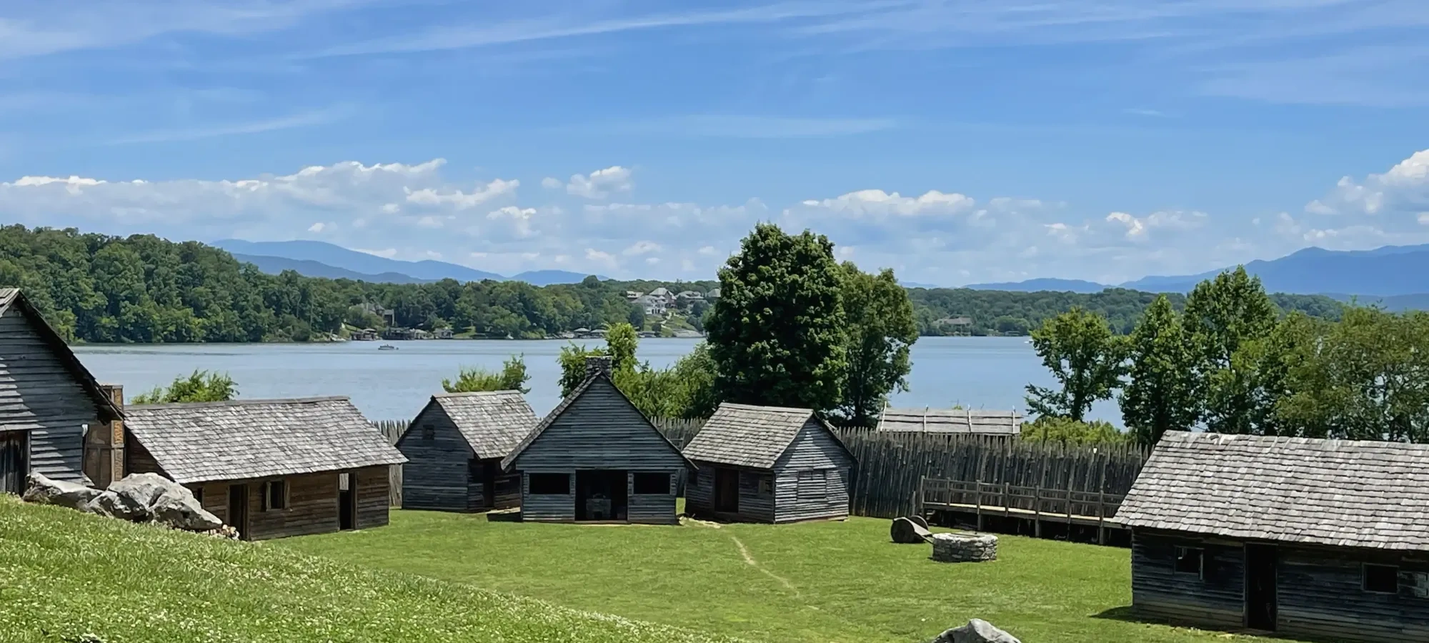 Historic wooden cabins by a lake under a clear blue sky.