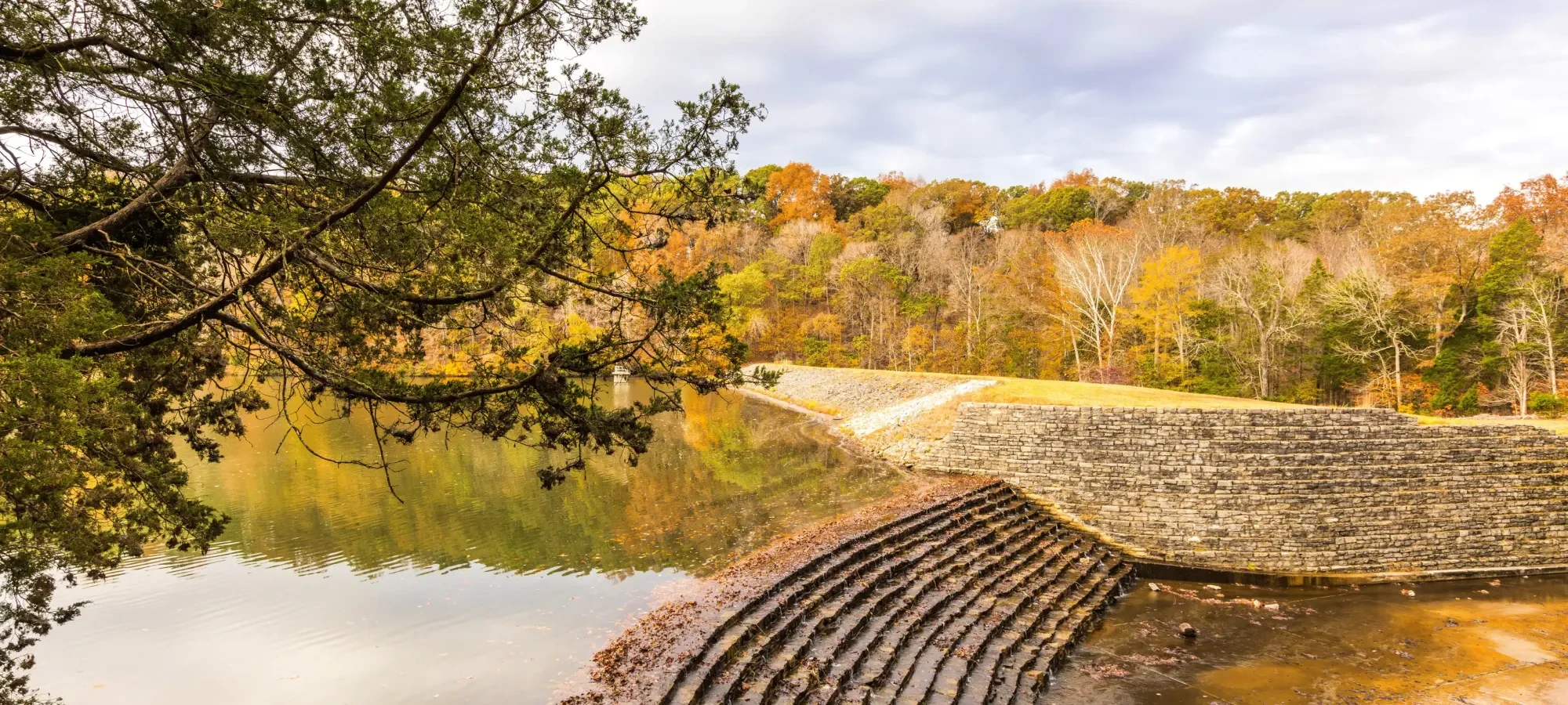 Stone steps by a lake with autumn trees reflected in water.