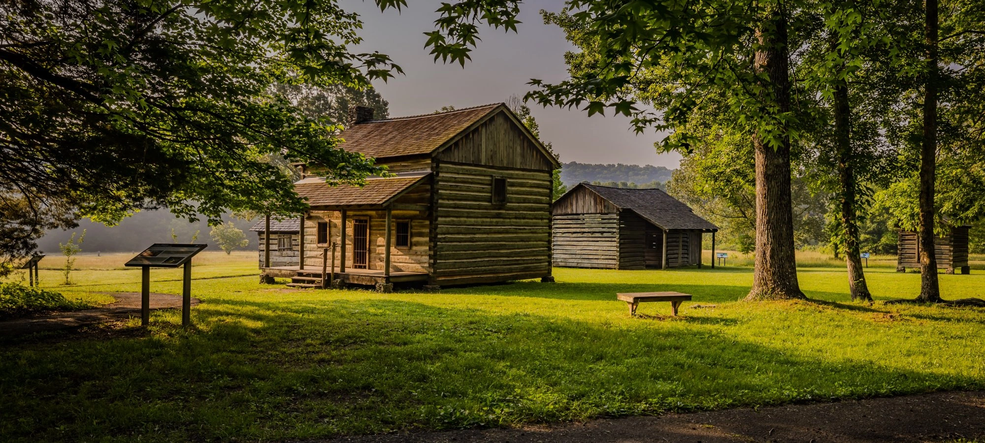 Log cabins in a grassy area with trees and a pathway.