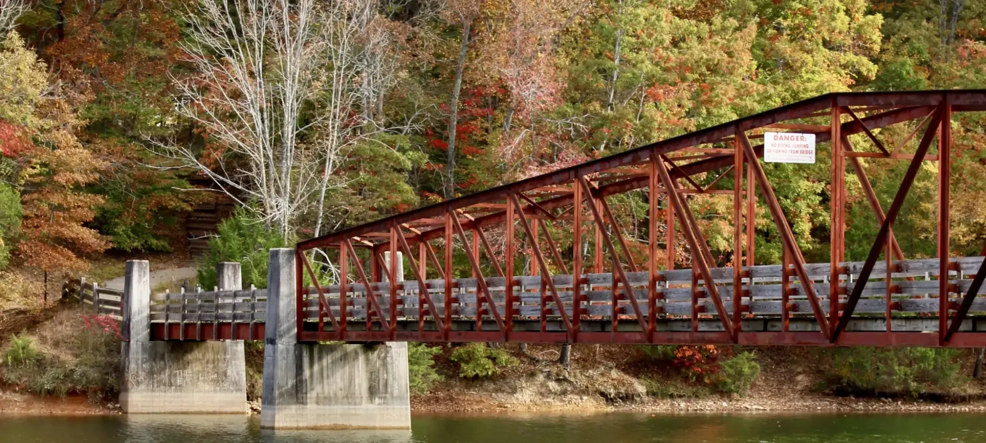 Red metal bridge over a river, surrounded by autumn trees.