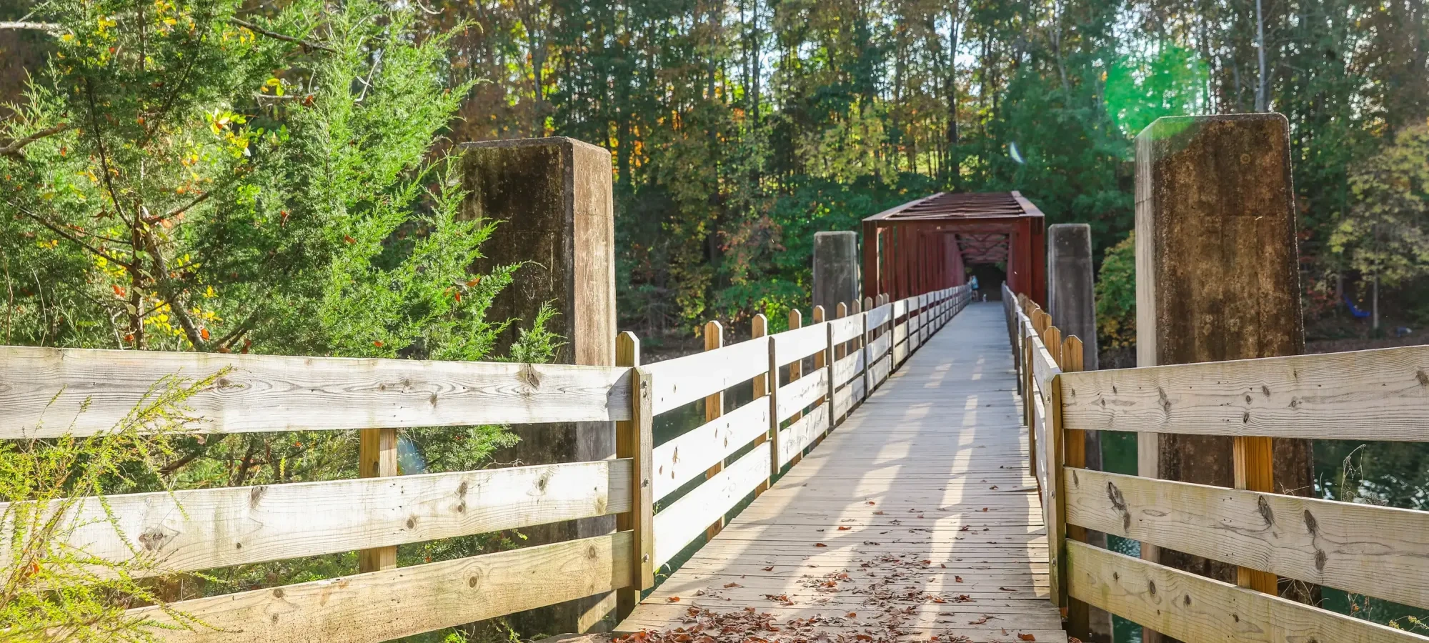 Wooden pathway leading to a covered bridge, surrounded by autumn trees.