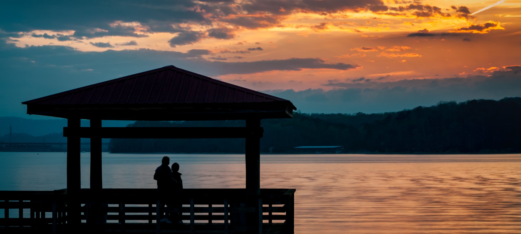 couple enjoying a beautiful sunset on the lake under a pavilion