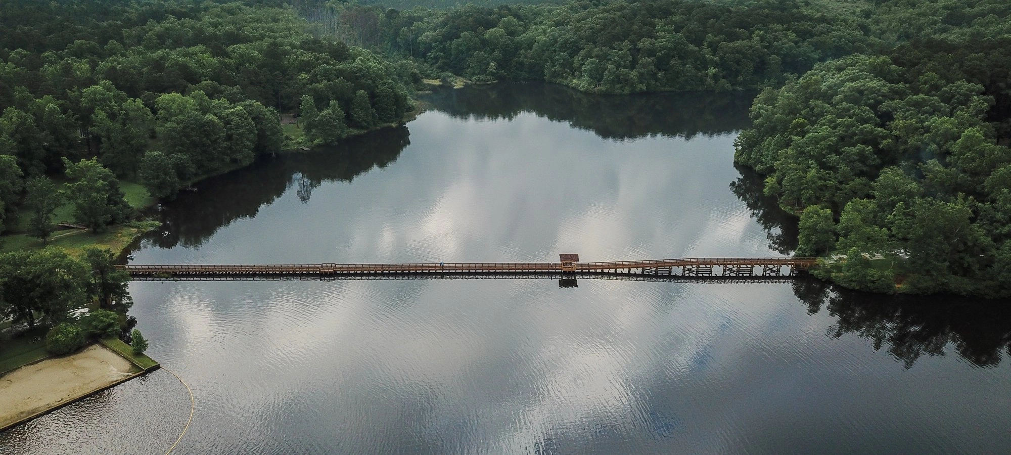 Wooden bridge over a calm lake surrounded by dense green forest.