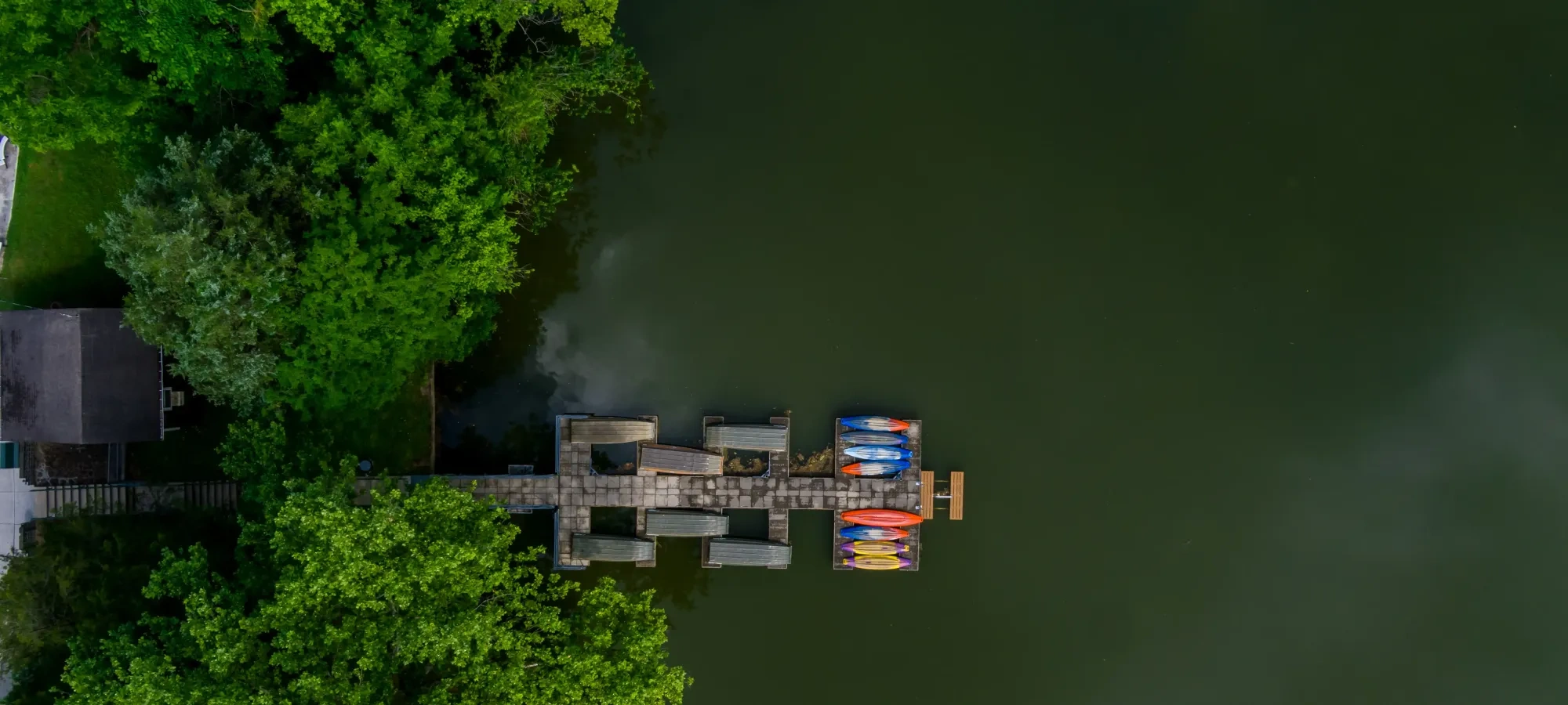 Kayaks on dock by lush green trees and dark water.