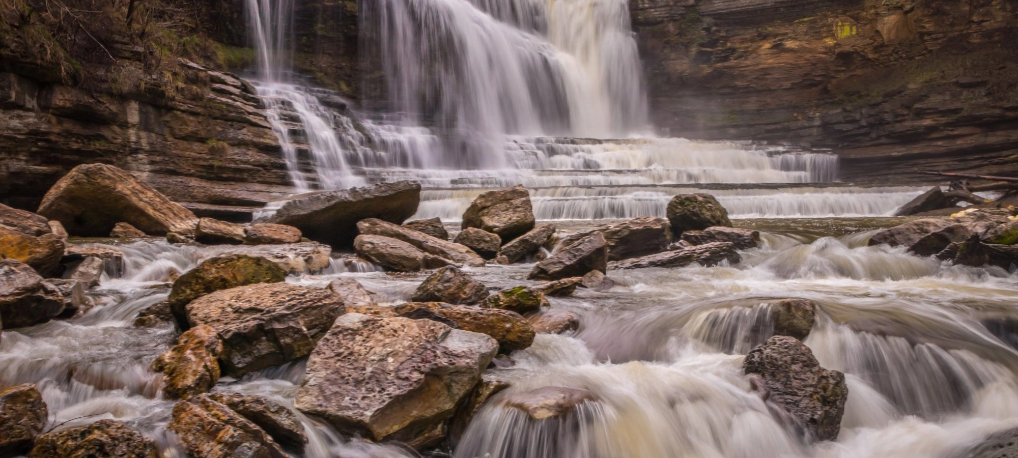 Waterfall cascading over rocky ledges with surrounding cliffs.