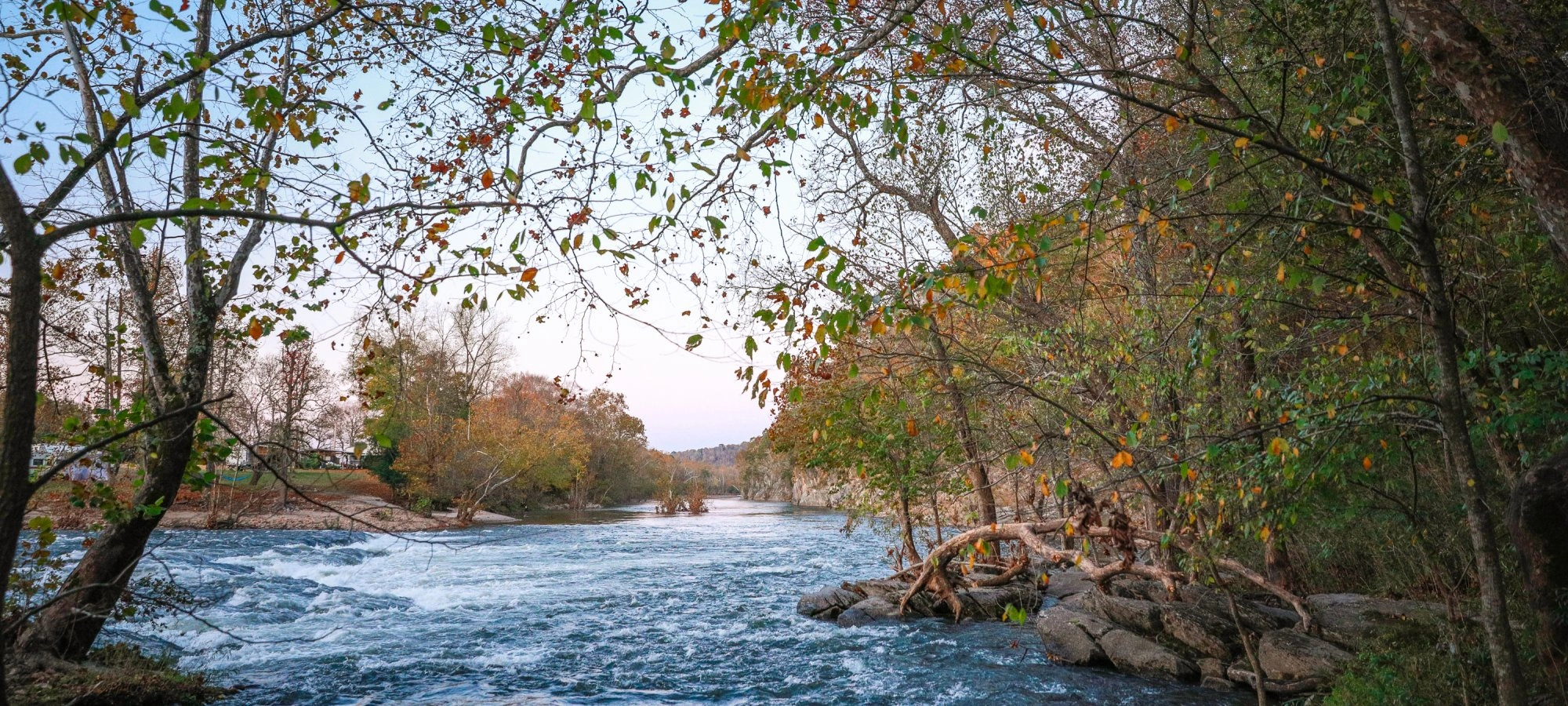 River with autumn trees on both sides, under a clear blue sky.