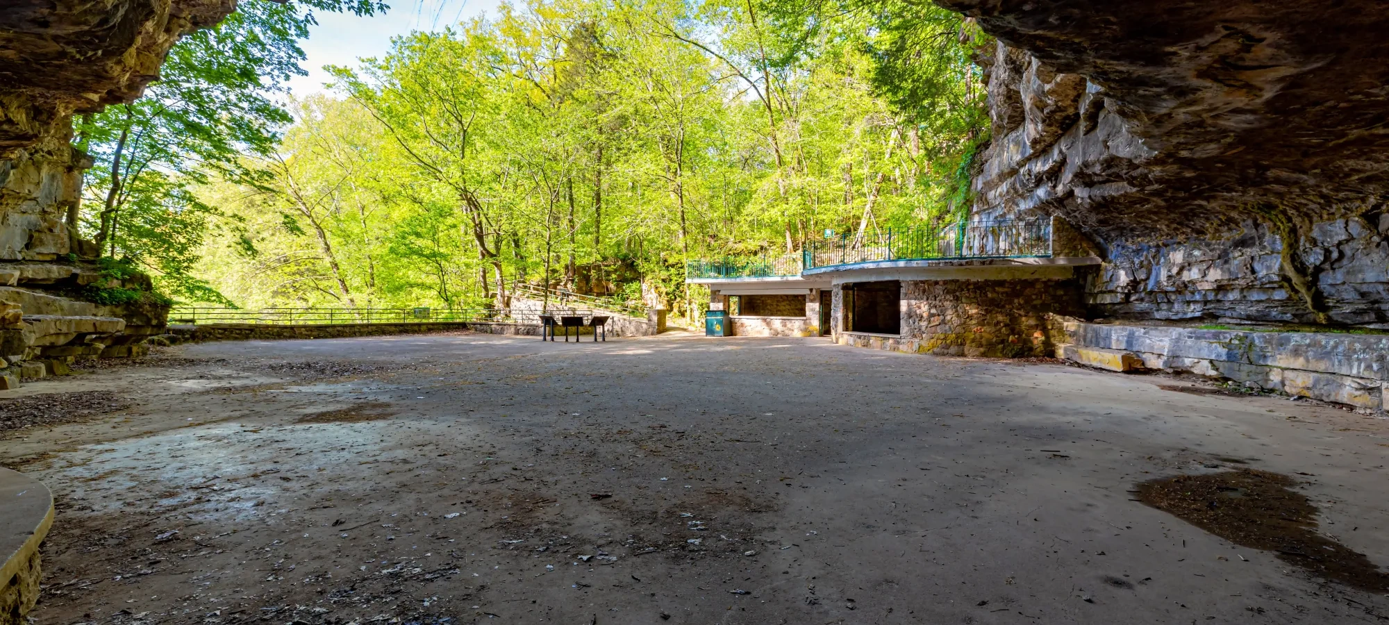 Cave foyer with rock walls, trees in the background, sunny day.